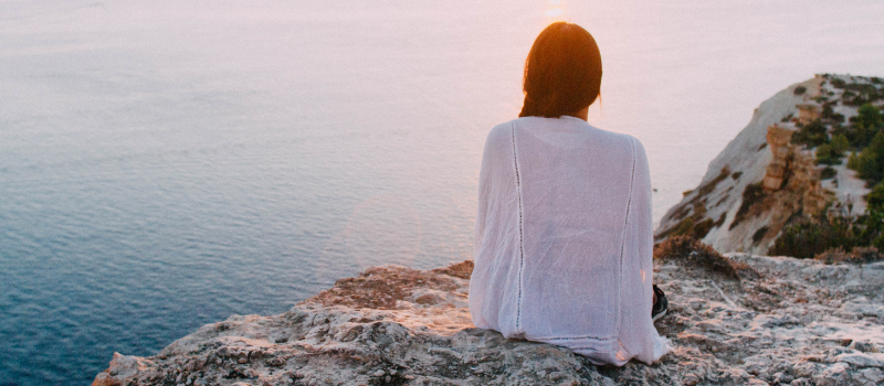 Woman self reflecting on a cliffside, overlooking the ocean. 